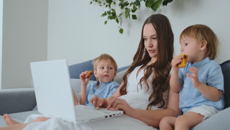 Beautiful-young-mom-and-two-little-kids-boys-are-looking-at-the-laptop-screen-family-photos.-And-make-online-shopping